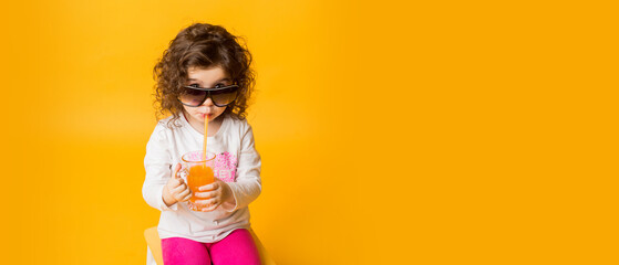 Beautiful girl enjoys drinking juice over yellow background