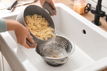 Woman pouring water from boiled pasta into colander in sink