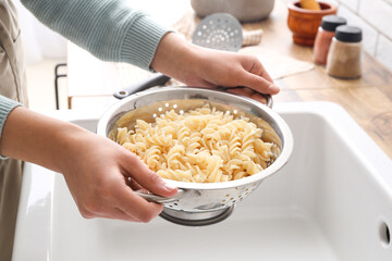 Woman holding colander with boiled fusilli pasta over sink, closeup