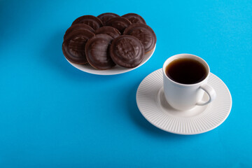 photo of a cup with a hot drink on a saucer next to a plate of cookies