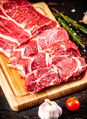 Raw beef on a wooden cutting board with rosemary.
