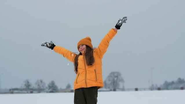 A happy teenager enjoying the snowfall. The girl is spinning in the snow and catching snow.