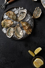 Open wet oysters on a plate with lemon and ice cubes and oysters knife, black background, top view