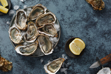 Huîtres fraiches, ouvertes dans une assiette avec des glaçons et citron sur un fond noir. Fruits de mer. Vue de dessus. 