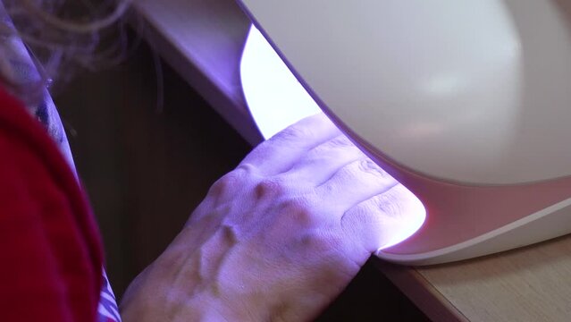 Woman dries her nails in uf lamp in beauty salon. Making manicure, nail art. 