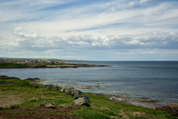 A rocky beach and grass, a village at a distance - Moray Firth