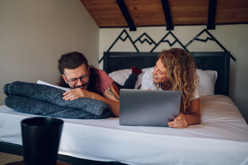 Romantic couple lying in the bed at home in the morning and using laptop