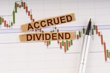 On the chart of business quotes lies a pen and torn paper with the inscription - ACCRUED DIVIDEND
