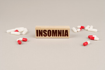 On a gray surface are tablets, capsules and a wooden plate with the inscription - Insomnia