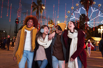 Colleagues walking around the amusement park at night with their arms around each other. A group of best friends hanging out together. Couples having fun and smiling. 