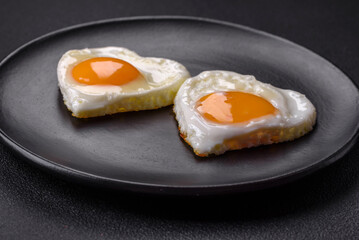 Two heart-shaped fried eggs on a black ceramic plate on a dark concrete background