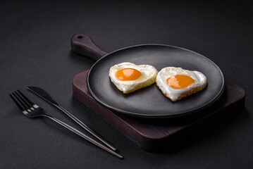 Two heart-shaped fried eggs on a black ceramic plate on a dark concrete background