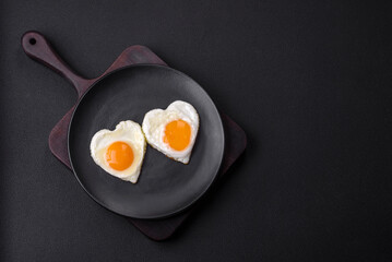 Two heart-shaped fried eggs on a black ceramic plate on a dark concrete background