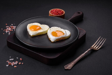 Two heart-shaped fried eggs on a black ceramic plate on a dark concrete background