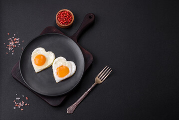 Two heart-shaped fried eggs on a black ceramic plate on a dark concrete background