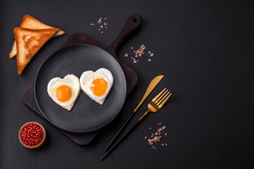 Two heart-shaped fried eggs on a black ceramic plate on a dark concrete background