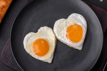Two heart-shaped fried eggs on a black ceramic plate on a dark concrete background