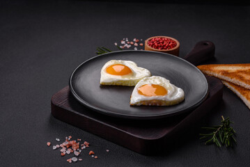 Two heart-shaped fried eggs on a black ceramic plate on a dark concrete background
