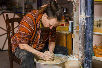 Professional male potter sitting and making clay cup on pottery wheel at workshop, studio. Handmade, art, handicraft concept