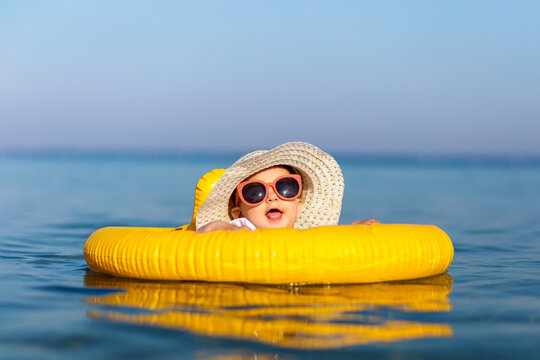 Cute little girl in ocean with swimming float, wearing sunglasses and sunhat. Children and summer season concept.