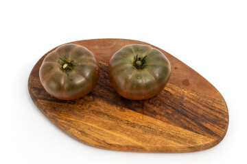 Two black tomatoes on wooden chopping board on white background isolated
