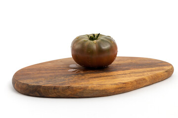 Black tomatoes on wooden chopping board on white background isolated