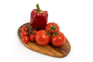 Red pepper and cherry tomatoes on wooden chopping board on white background isolated