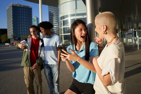 Multiracial people having fun together watching cell phone screens outdoors. Gen Z young students using smartphone and social networks together. High quality photo