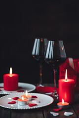 Saint Valentine's Day celebration. Red burning candles, hearts, gift box, postcard on dark wooden background. Happy holiday . Table decor for festive dinner, romantic atmosphere. Copy space for text