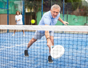 Naklejka premium Portrait of emotional aged man enjoying friendly padel tennis match at outdoors court