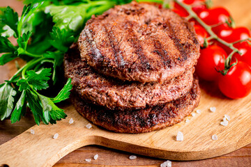 Burger grill on a cutting board with greens and tomatoes. 