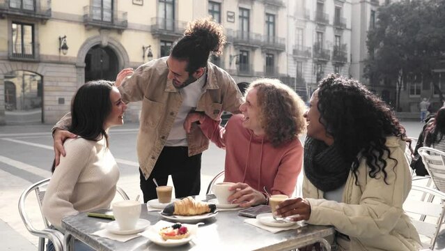 Group of friends meet in the street. People having breakfast outdoors on a terrace on the city street. Man greets his college. High quality photo