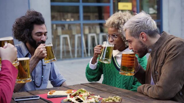Friends drinking beer at terrace outdoors on weekend. Friendship concept with young people having fun together toasting brew pint on happy hour at pub. High quality photo