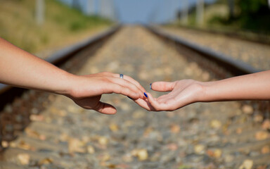 a man's hand holds a woman's hand, in the background a blurred view of the railway. walk of a couple in love along the railroad tracks. concept of joint seed of life and love