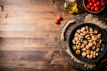 Frying pan with fried mushrooms on a wooden tray. 