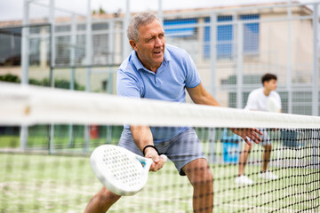 Portrait of elderly man playing paddle tennis with friends on open court. Active lifestyle concept