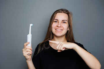 Portrait of a smiling young woman without makeup in a black t-shirt brushing her teeth, mature woman, natural beauty concept. Morning brush for teeth, dental ultrasonic brush.