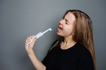 Obraz premium Portrait of a smiling young woman without makeup in a black t-shirt brushing her teeth, mature woman, natural beauty concept. Morning brush for teeth, dental ultrasonic brush.
