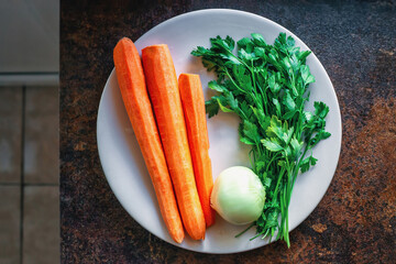 Fresh vegetables on white ceramic plate, top view. Peeled carrots, onions and green parsley on table