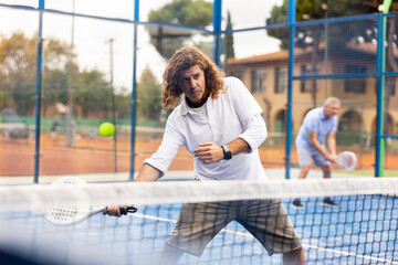 Portrait of sporty resolved man playing padel on open court on summer day, ready to hit ball....