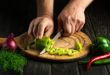 The cook hands with a knife cut fresh pepper on the cutting board of the restaurant kitchen. Vegetarian diet. Copy space