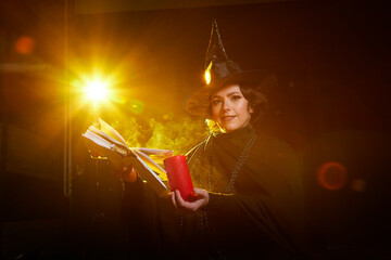 Portrait of cute young witch in pointed hat with candle wand in her hands and black background. Girl or Woman in Halloween costume during party. Model posing in photo shoot
