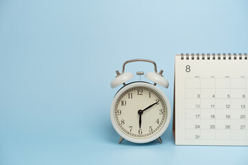 Naklejka premium close up of calendar and alarm clock on the blue table background, planning for business meeting or travel planning concept