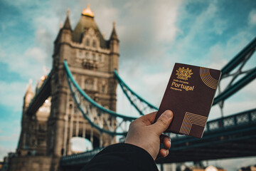 London, UK - 2023: Hand holding a portuguese passport in front of the Tower Bridge.
