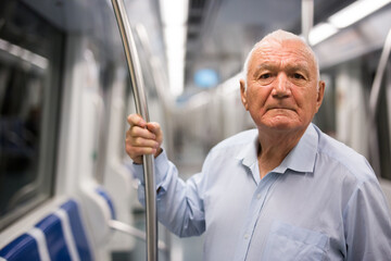 Fototapeta na wymiar Elderly caucasian man standing in subway car and holding handrail while waiting for his station.
