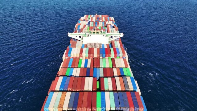 Aerial drone video of container ship with colourful truck size containers cruising in open ocean Mediterranean Aegean sea, Greece
