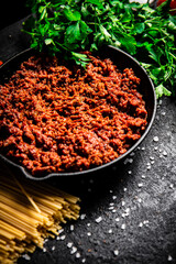 Bolognese sauce in a frying pan with pasta dry and parsley. 