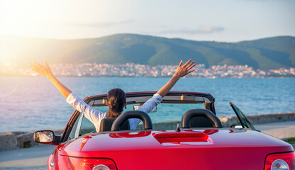 Woman in red cabriolet car at background of sea water. Travel, freedom and holidays concept.