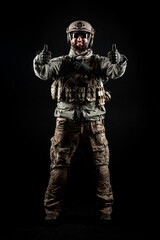 USA soldier in a military suit with a rifle smiles and shows a like against a dark background, American commando in uniform