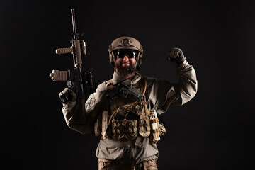 USA soldier in a military suit with a rifle smiles and shows strength against a dark background, an American commando in uniform